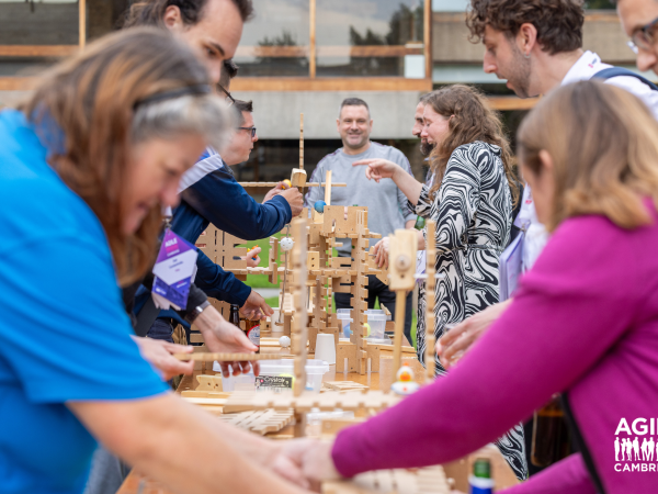 A group of people gather around a team building activity. They are trying to build a wooden structure out of planks