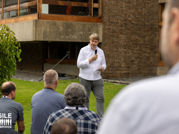 A speaker stands in front of an audience, they are outside on a green lawn